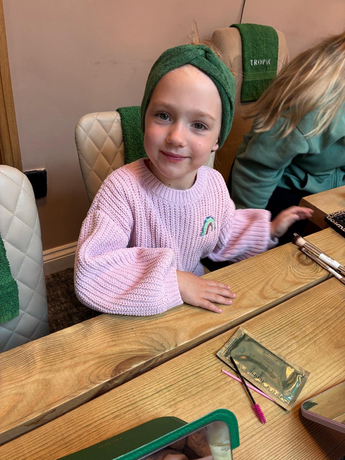 A young girl with a Tropic towel wrap smiling during a mini facial experience
